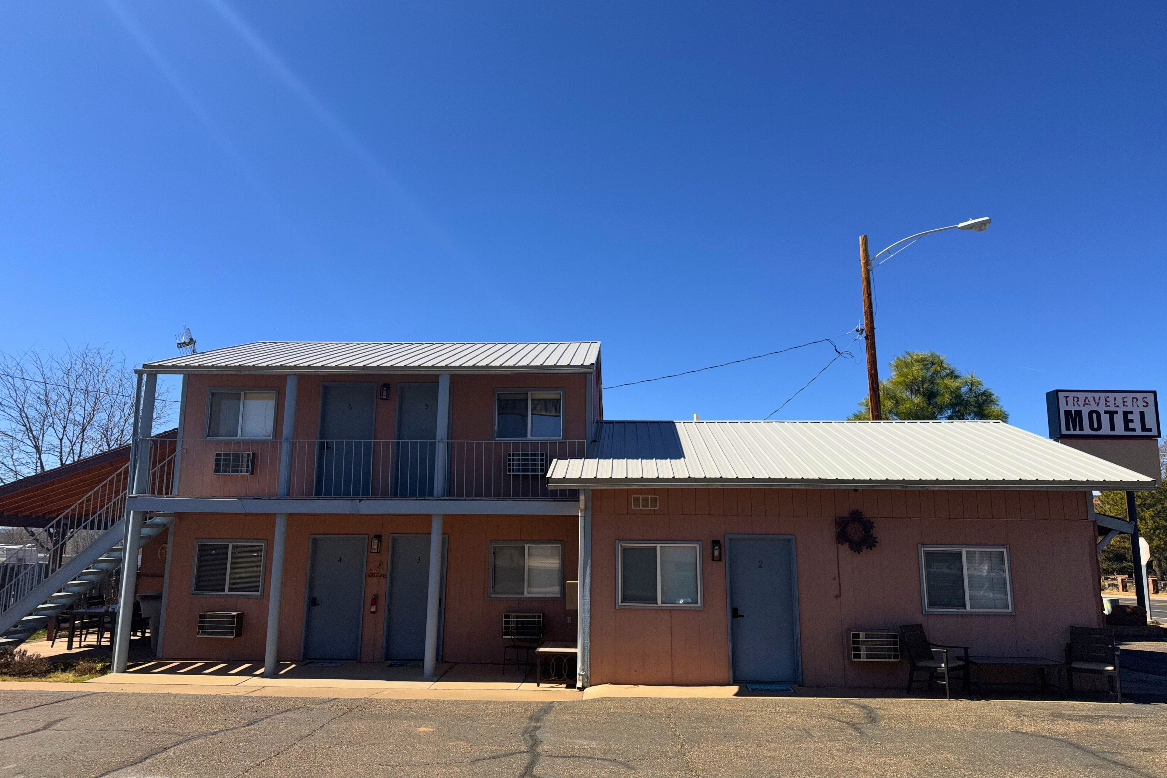 A two-story motel with a balcony on the upper floor, a sign reading "Travelers Motel," and a small porch area with a bench.
