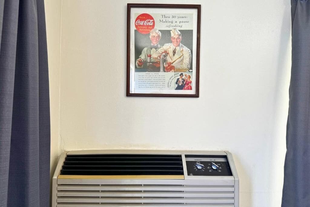 A framed advertisement on a wall above a wall-mounted air conditioner.