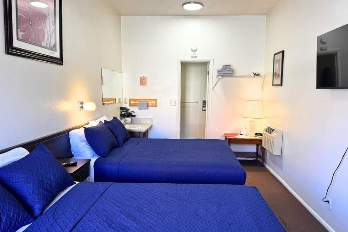 Habitación de hotel con dos camas, un escritorio, un espejo, un televisor y una puerta que da a un baño.