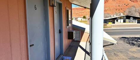 A building with a porch, numbered doors, and a view of a red rock formation in the background.