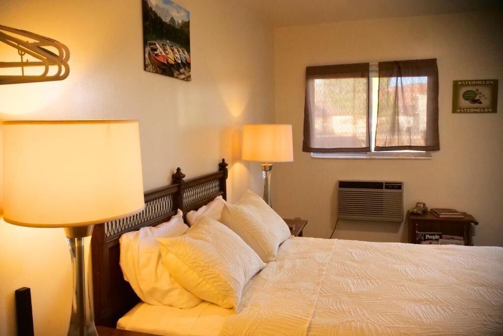 A neatly made bed with white linens, a wooden headboard, and two bedside lamps.