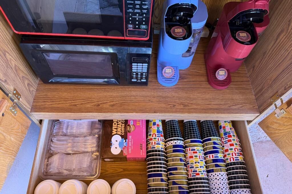 A drawer with a microwave, coffee makers, and a variety of colorful mugs.