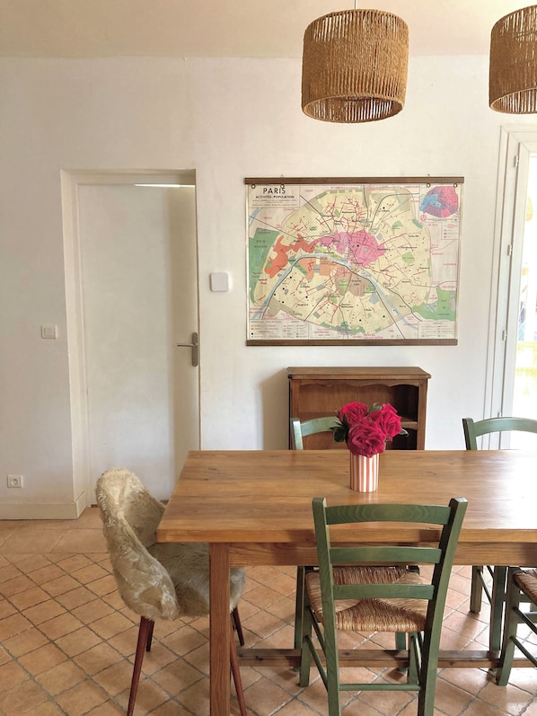 A dining area with a wooden table, green chairs, a vase with flowers, and a map of Paris on the wall.