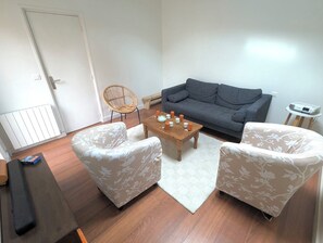A living room with a grey sofa, two white armchairs, a wooden coffee table, and a small side table with a projector.