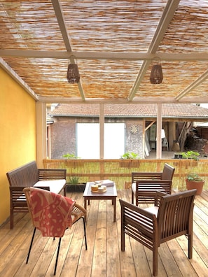 A covered outdoor seating area with wooden furniture and a view of a building with a tiled roof.