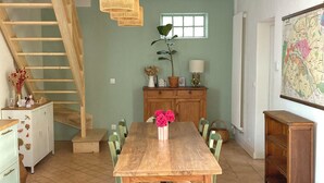 Ein Essbereich mit einem Holztisch und Stühlen, einer Treppe, einem Schrank mit Blumenvase und einer Karte an der Wand.
