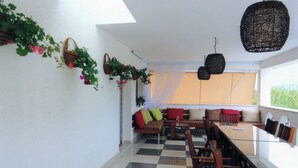 A spacious balcony with a checkered floor, a sofa with cushions, and hanging baskets with greenery.