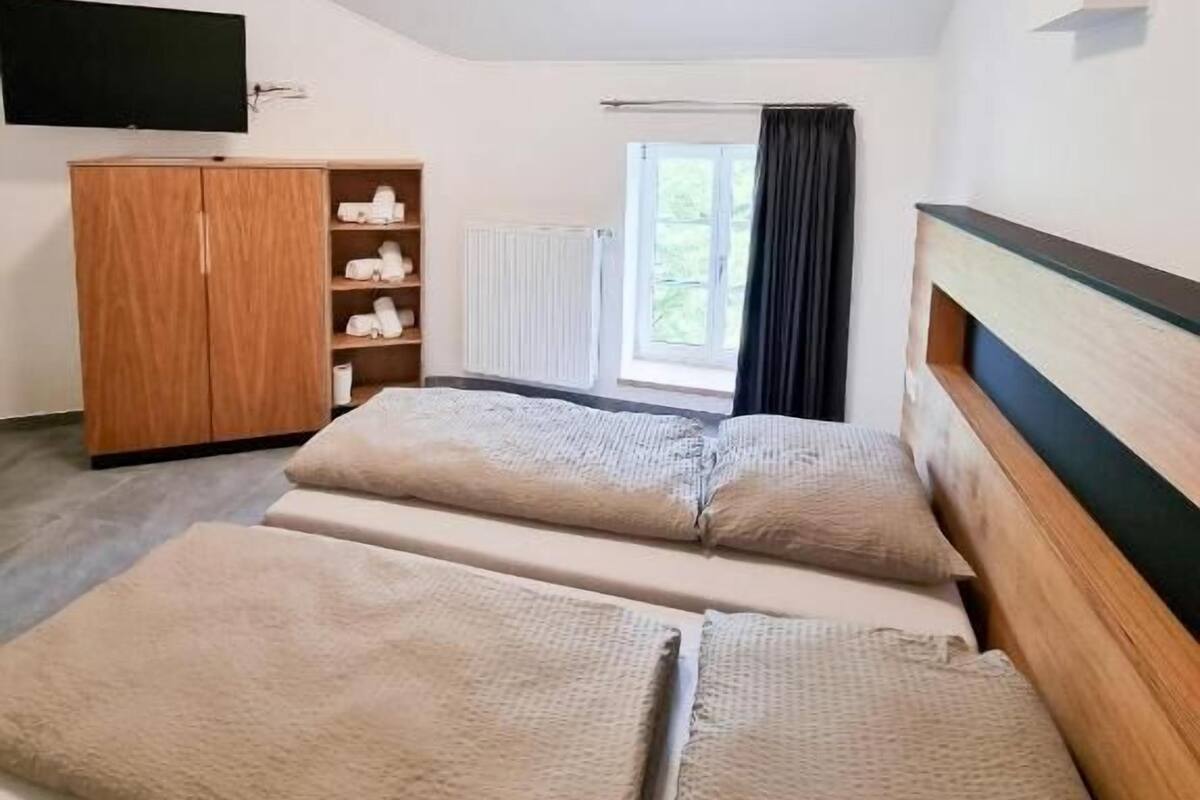 A room with two beds, a wardrobe, a TV, and a window with curtains.