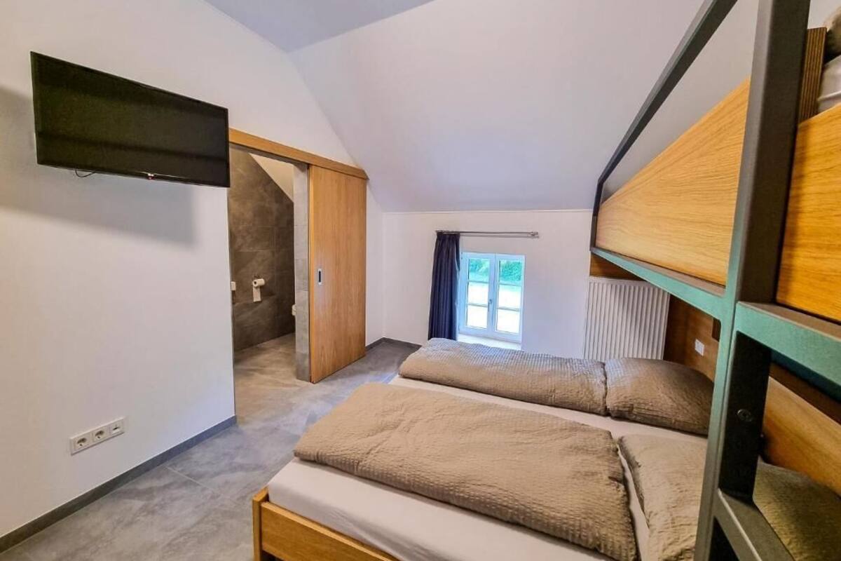 A bedroom with a bunk bed, a flat-screen TV mounted on the wall, and a window providing a view of the outdoors.