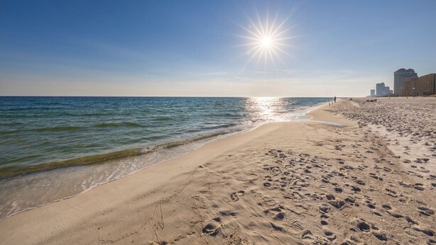 Una spiaggia con impronte, cielo sereno e edifici sullo sfondo.
