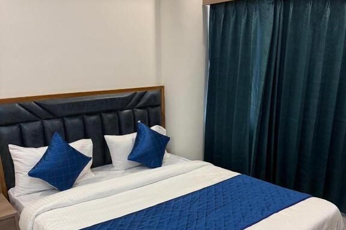 A neatly made bed with a blue quilt and white bedding, a wooden headboard, and a dark blue curtain.