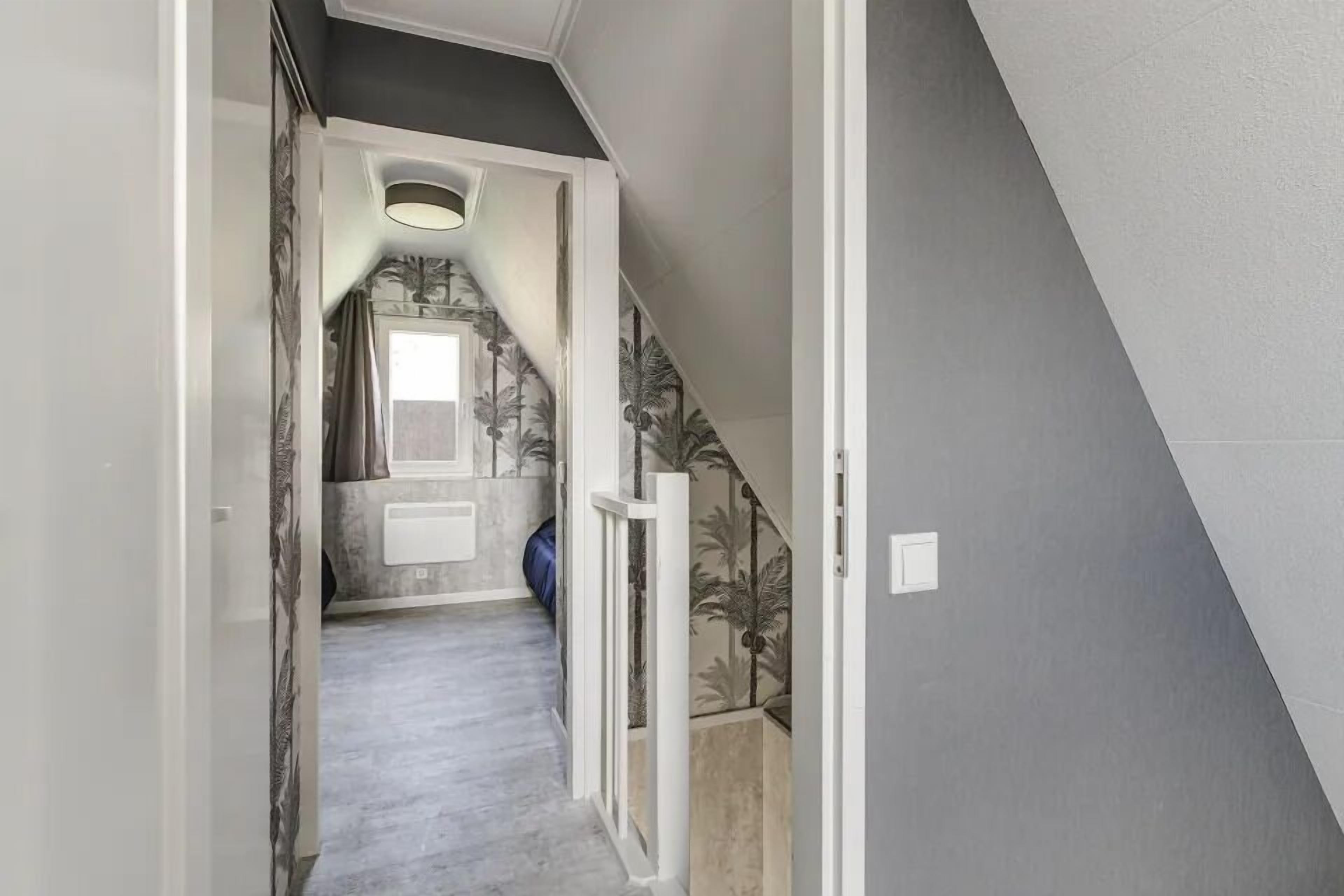 Een hal met een trap die naar een kamer leidt, witte muren en een grijze vloer.