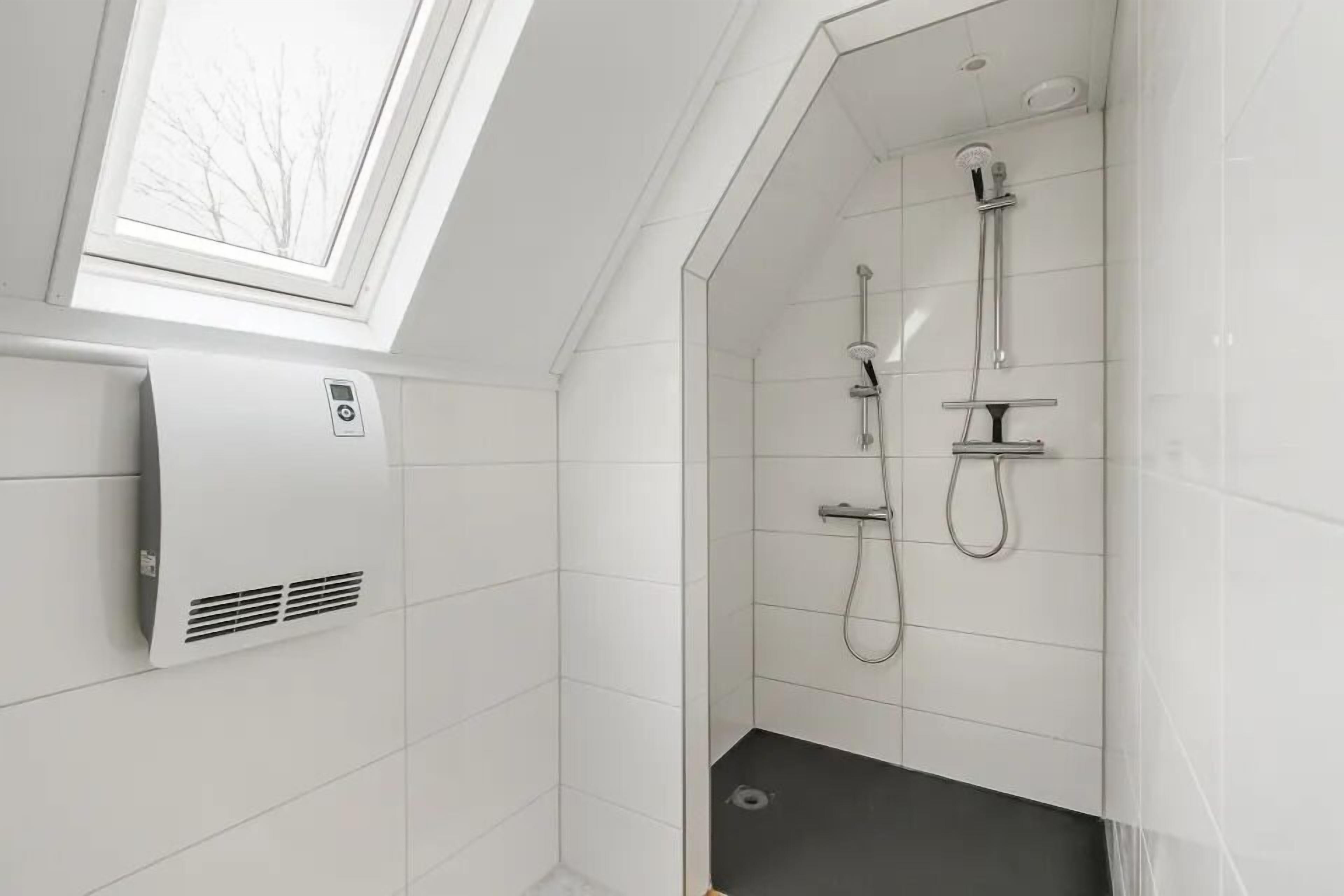 Eine moderne Dusche mit Dachfenster, weißen Fliesen und einer Wandbedienung.
