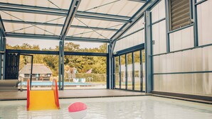 Une piscine intérieure avec un toboggan, des murs en verre et une vue sur l’extérieur.