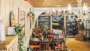 L’intérieur d’un restaurant avec des murs en bois, de nombreuses tables et chaises, des luminaires suspendus et un menu écrit à la craie sur un tableau noir.