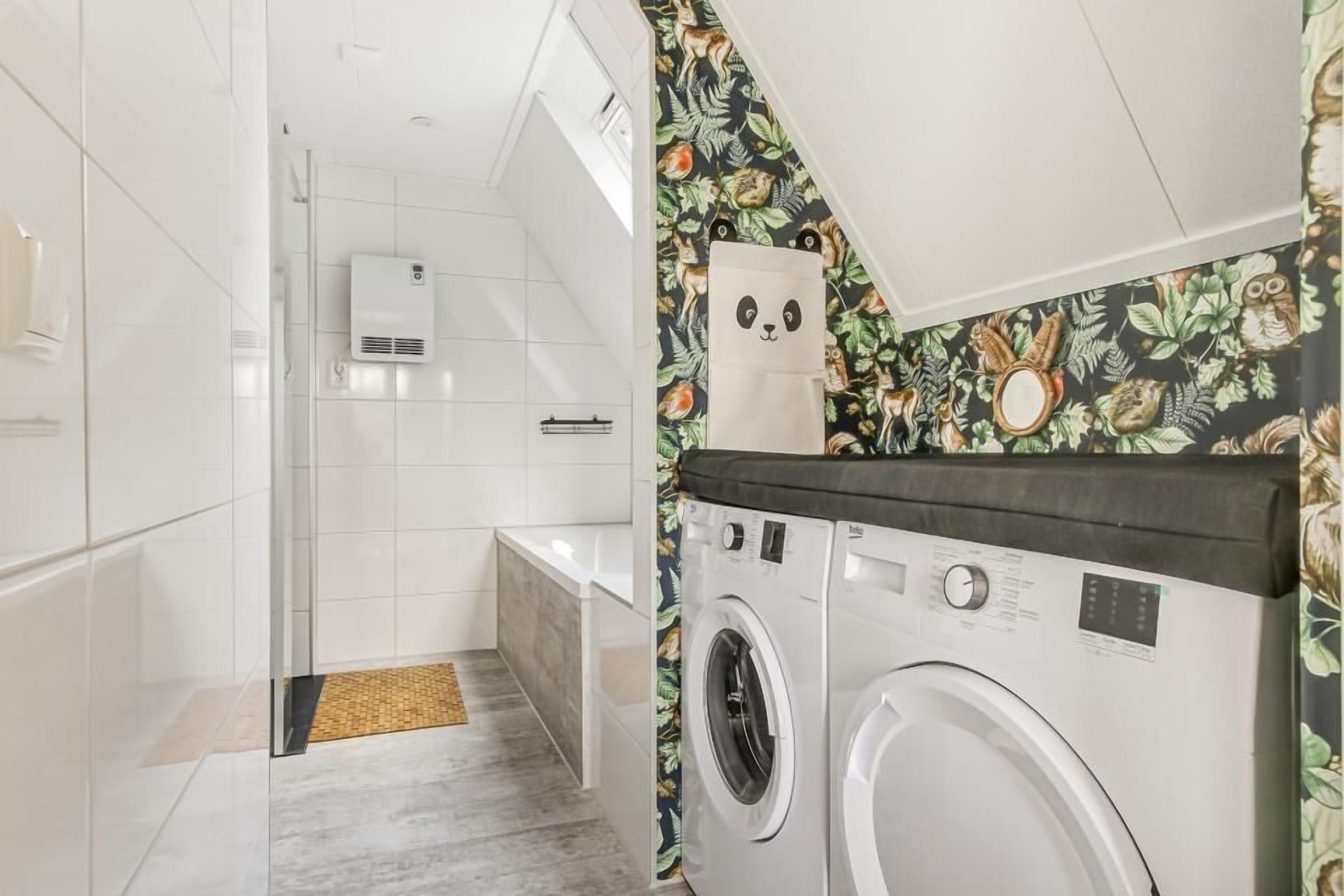Une buanderie moderne équipée d’un lave-linge et d’un sèche-linge, d’une cabine de douche en verre et d’un mur orné d’un motif.