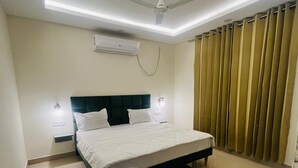 A modern bedroom with a bed, ceiling fan, air conditioning unit, and curtains. - Olivine By Housiify (Gurugram)