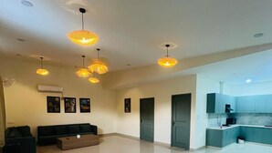 A spacious living area with a modern kitchen, a sofa set, and pendant lighting. - Olivine By Housiify (Gurugram)