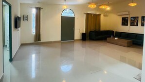 A spacious living area with a polished floor, a dark-colored sofa set, and pendant lighting fixtures. - Olivine By Housiify (Gurugram)