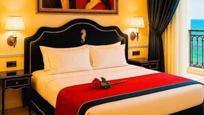 Habitación de hotel con una cama grande, dos mesitas de noche con lámparas, un cuadro sobre la cama y vistas al mar a través de una ventana con cortinas.