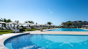 Ein Swimmingpool mit Liegestühlen und Sonnenschirmen, umgeben von Palmen und Gebäuden.