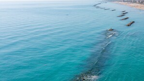 Küstensicht mit blauem Himmel, ruhigem Meer und einer fernen Uferlinie mit Gebäuden.
