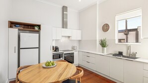 A modern kitchen with white cabinetry, a wooden dining table, and a built-in oven. - Light-Filled North Perth Stay | Walk to Cafes | Stylish & Central (North Perth)