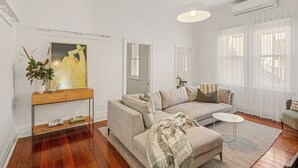 A modern living room with a beige sofa, a small round table, and a large window with sheer curtains. - Light-Filled North Perth Stay | Walk to Cafes | Stylish & Central (North Perth)