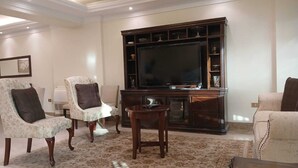 Ein Wohnzimmer mit einem großen Flachbildfernseher, zwei Sesseln, einem Couchtisch und einem Sofa.