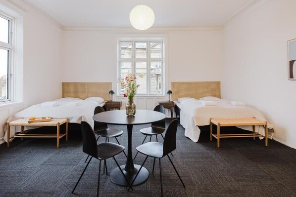 Habitación de hotel con dos camas, una mesa de comedor con sillas, un florero con flores y una ventana con vistas.
