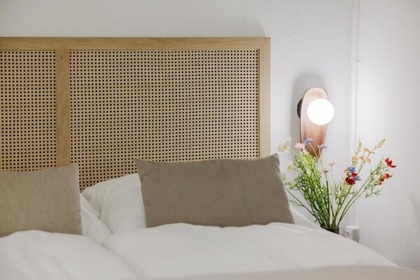 Una cama con cabecera de madera, un espejo en la mesita de noche y una planta en maceta con flores.