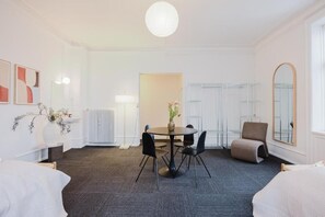 Una habitación de hotel moderna con una mesa redonda de comedor, sillas negras, un sofá, un espejo grande y un radiador.