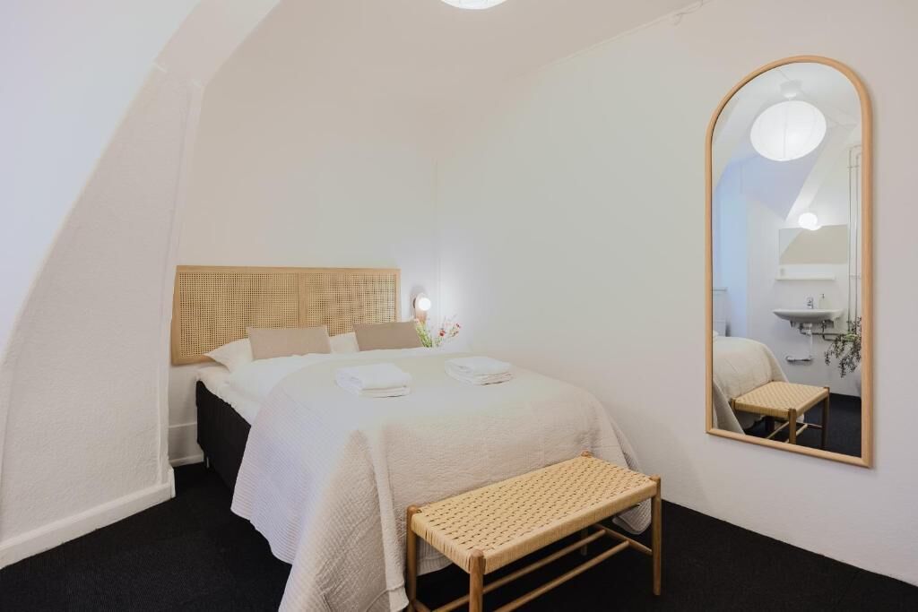 Un dormitorio con cama, un banco, un espejo y cabecero.