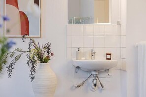 Un baño con un lavabo blanco, un espejo y un cuadro abstracto enmarcado en la pared.