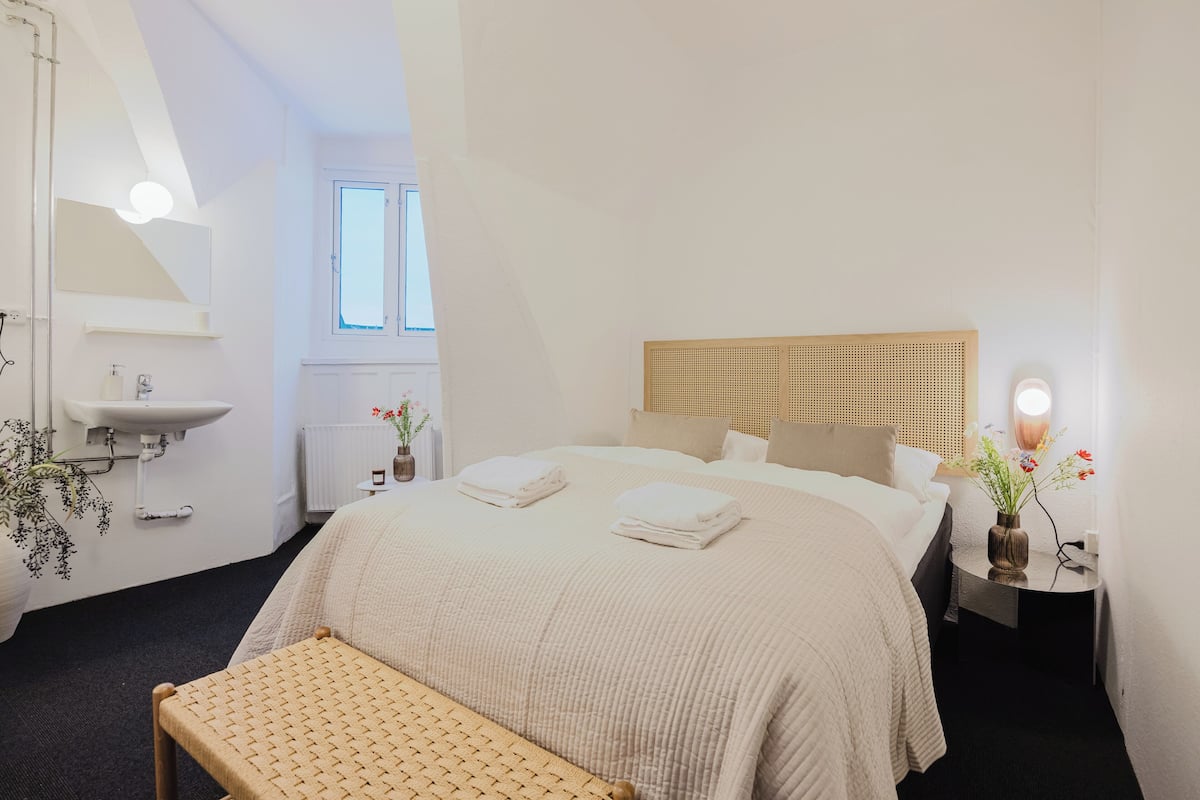 Un dormitorio con cama, mesita de noche, lámpara y ventana.