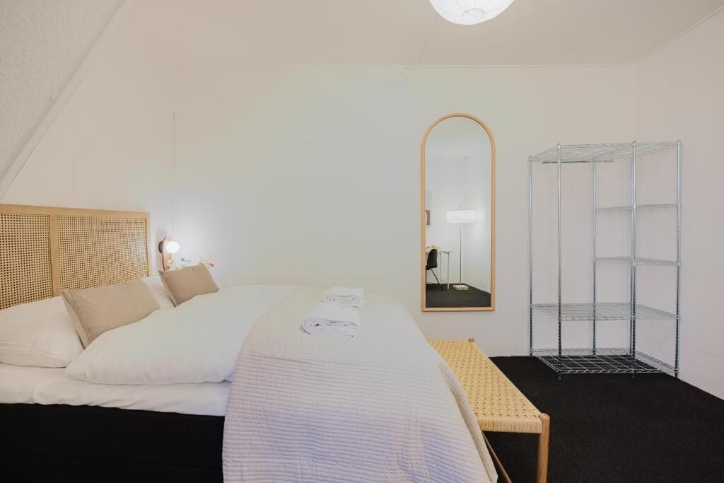 A hotel room with a bed, a bench, a mirror, and a metal shelving unit.