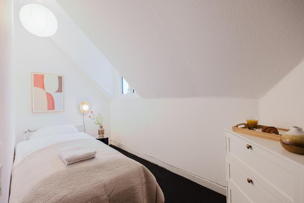 Un dormitorio con cama, mesita de noche, lámpara y una ventana pequeña.