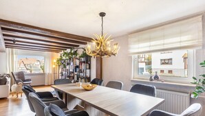 Un comedor con una mesa larga, sillas, una araña y vistas al exterior.