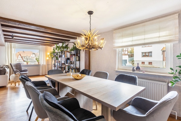 A dining area with a long table, chairs, a chandelier, and a view of the outside.