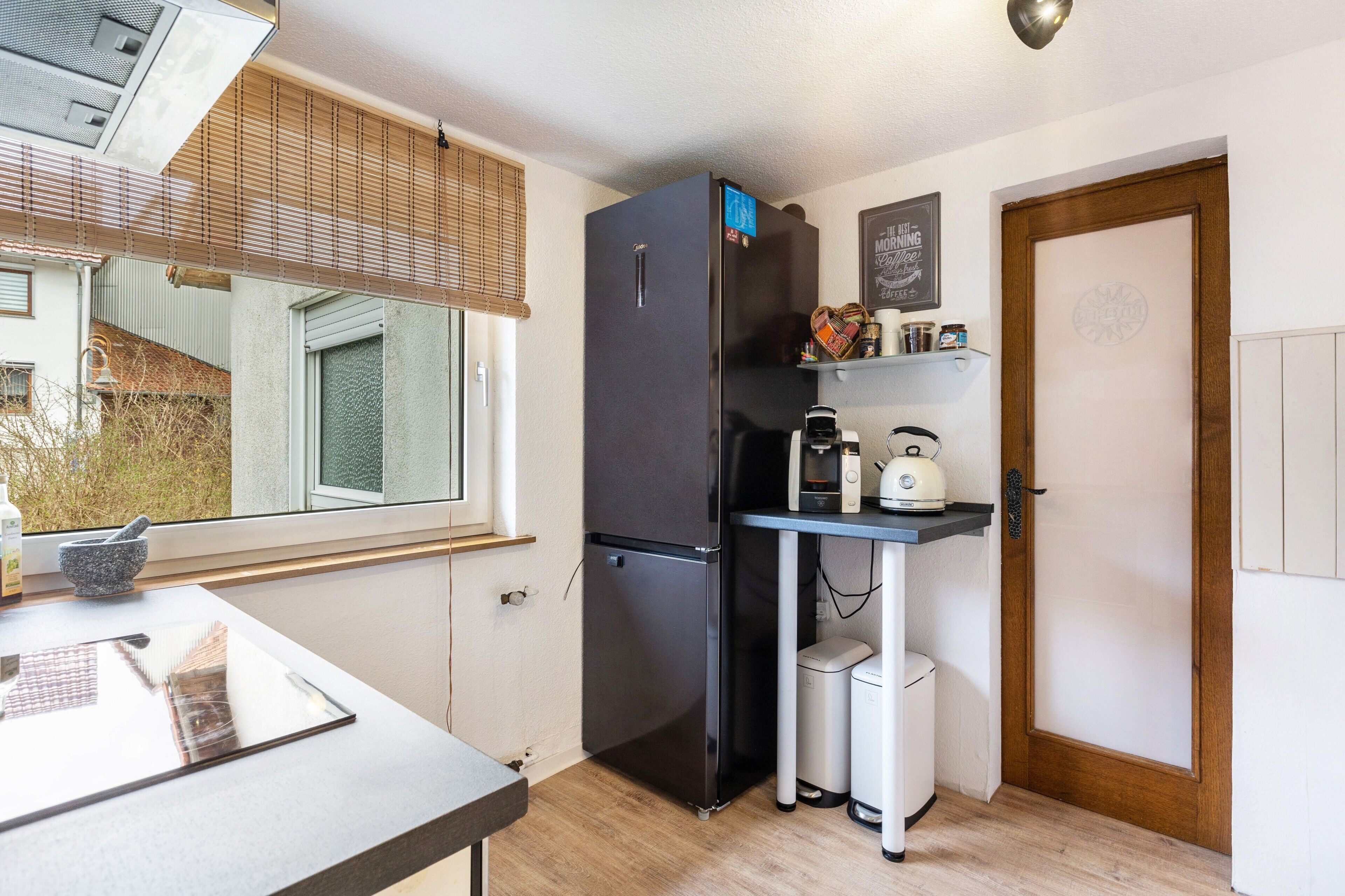 A compact kitchen with a refrigerator, coffee maker, and a small trash bin.