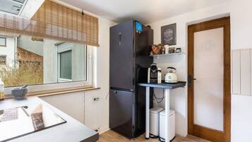 A compact kitchen with a refrigerator, coffee maker, and a small trash bin.