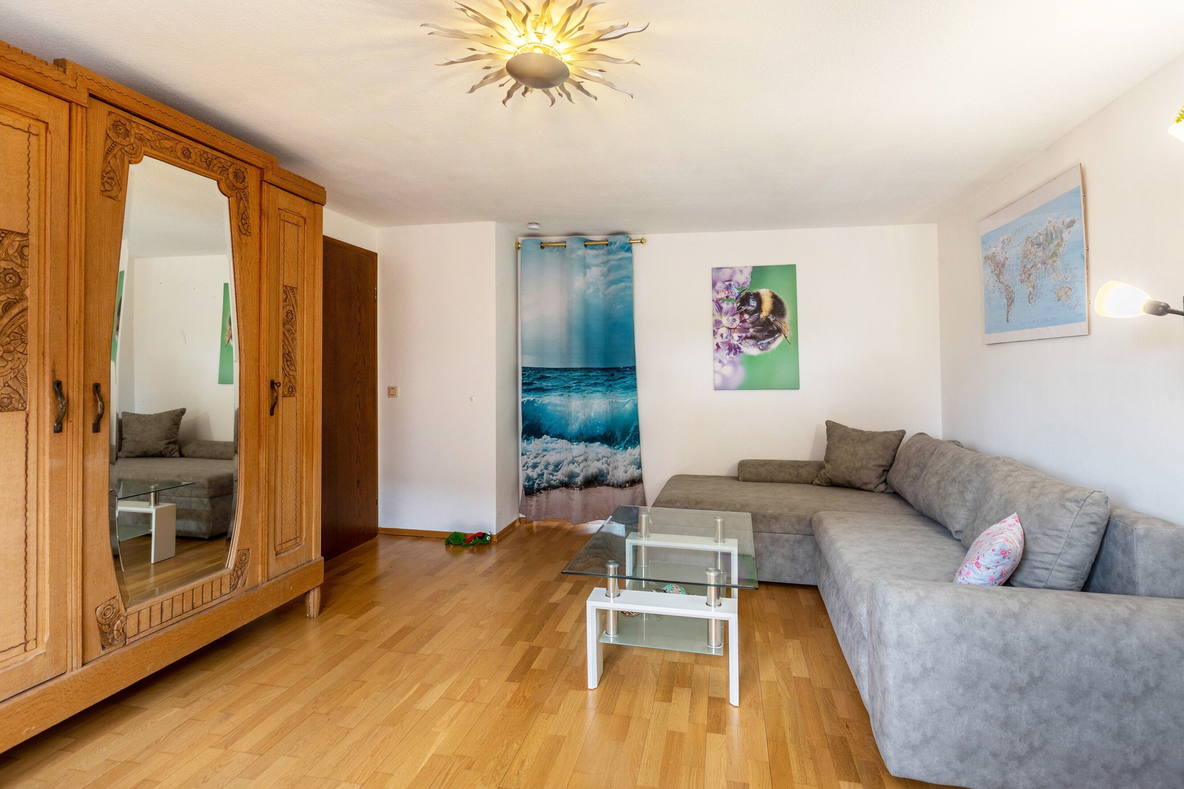 A living room with a wooden wardrobe, a grey sofa, a glass coffee table, and a large mirror.