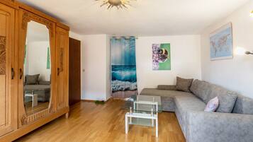 A living room with a wooden wardrobe, a grey sofa, a glass coffee table, and a large mirror.
