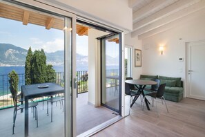 Ein Balkon mit Tisch und Stühlen, ein grünes Sofa und eine Tür zu einem Zimmer mit Blick auf Meer und Berge.
