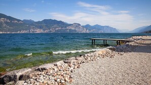 A rocky shoreline with a pier extending into calm waters, surrounded by mountains. - Pèler Apartment: Modern Elegance, Stunning Views and Comfort in Brenzone (Castelletto)