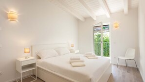 A bedroom with a bed, bedside tables, a chair, and a window with a view of greenery. - Pèler Apartment: Modern Elegance, Stunning Views and Comfort in Brenzone (Castelletto)