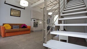 Um interior moderno com uma escada, um sofá com almofadas e uma área de cozinha.