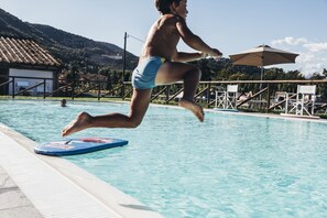 A person jumping into a swimming pool with a blue kickboard, surrounded by lounge chairs and umbrellas. - Tenuta San Giovanni - Orange Apartment (lucca)