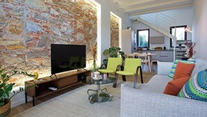 A living room with a stone wall, a flat-screen TV, a glass coffee table, and a sofa with colorful cushions.