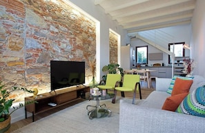 A living room with a stone wall, a flat-screen TV, a glass coffee table, and a sofa with colorful cushions. - Casa Josephina, Charming Loft near Lucca's Centre (Lucca)